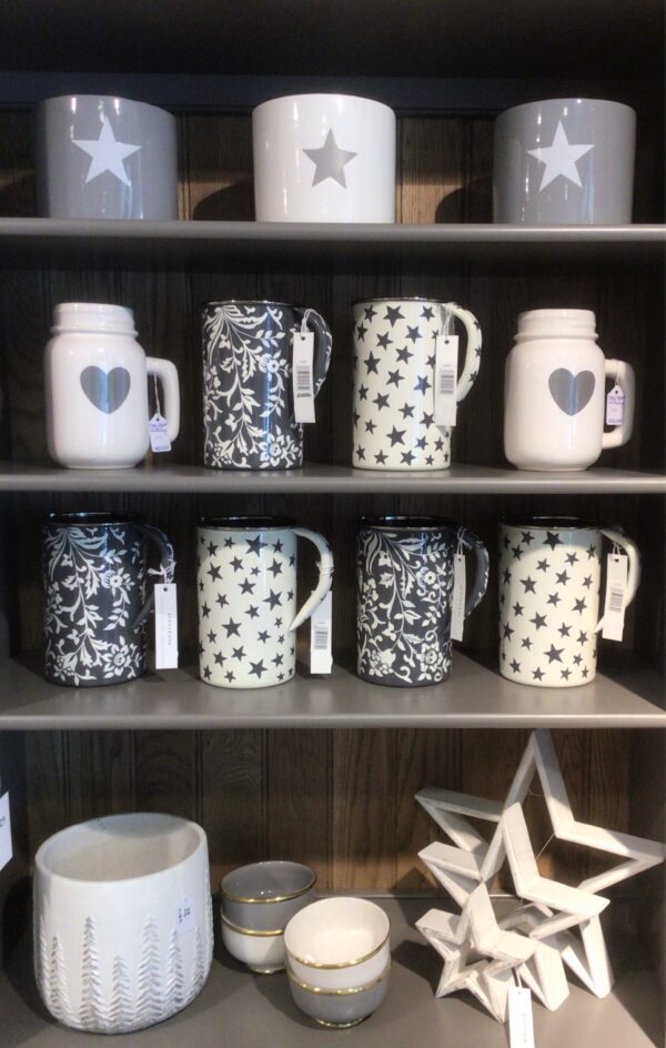 Grey dresser with open shelving. Styled on the open shelving are various enamel jugs styled on open shelving. Grey with white floral design. White with grey star motif. White with grey heart mason style jug. Set of three white stars.